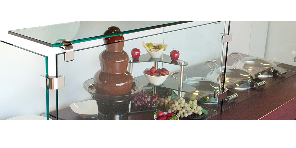 Chocolate fountain displayed with other buffet enhancing products behind a tempered glass sneeze guard.